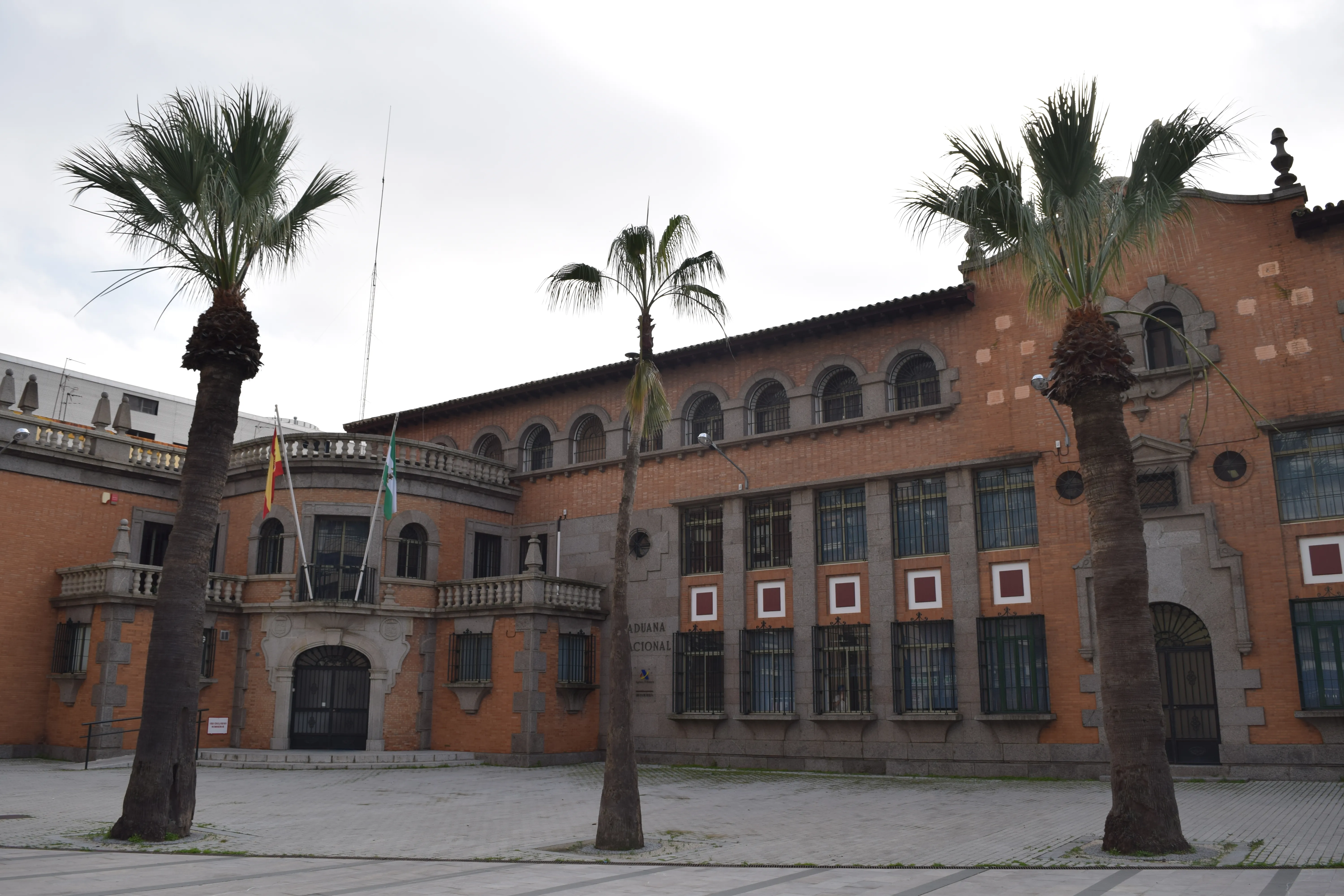 Edificio histórico de la Agencia Tributaria en Huelva, antigua aduana de ladrillo con palmeras delante
