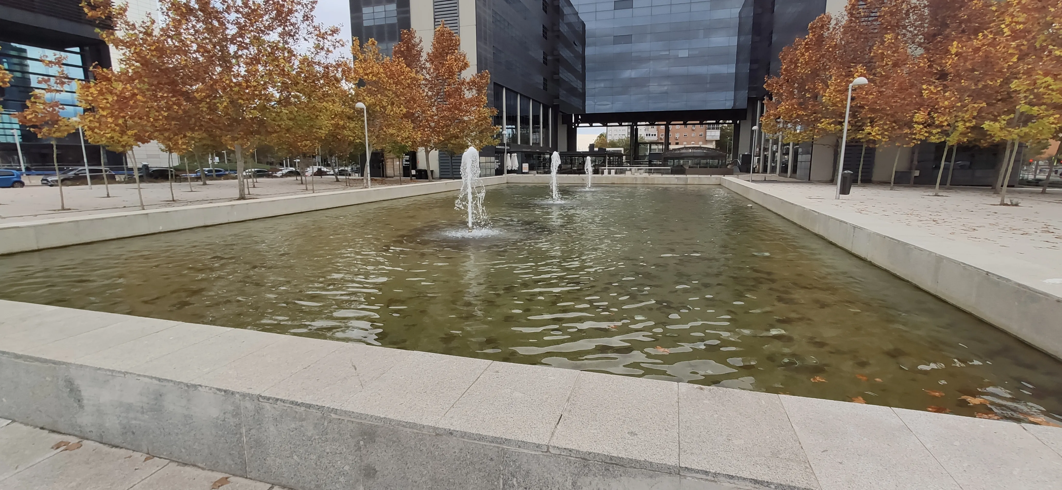 Plaza con estanque y surtidores frente a edificios de oficinas en el área financiera de Madrid, árboles en otoño a ambos lados