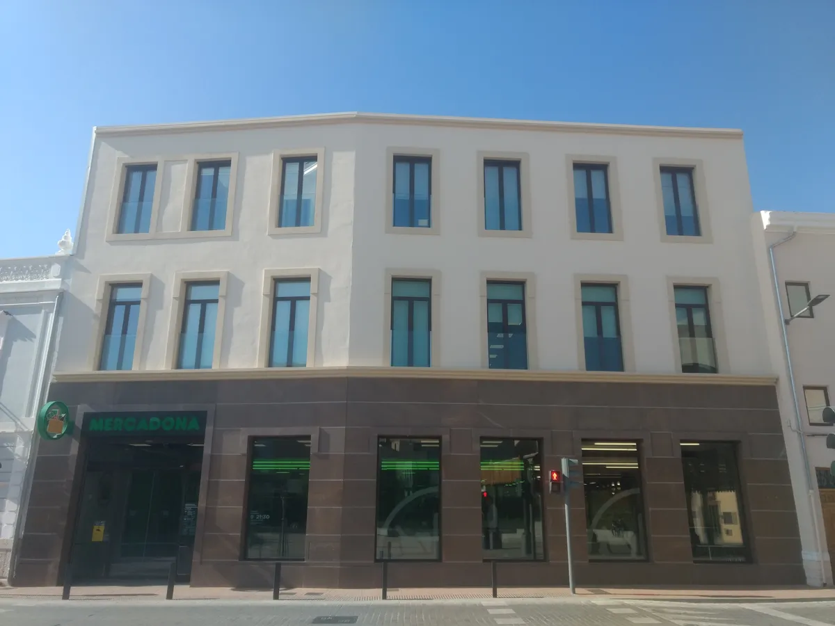 Fachada de un supermercado Mercadona en un edificio rehabilitado con planta baja en piedra oscura y rótulo verde sobre la entrada