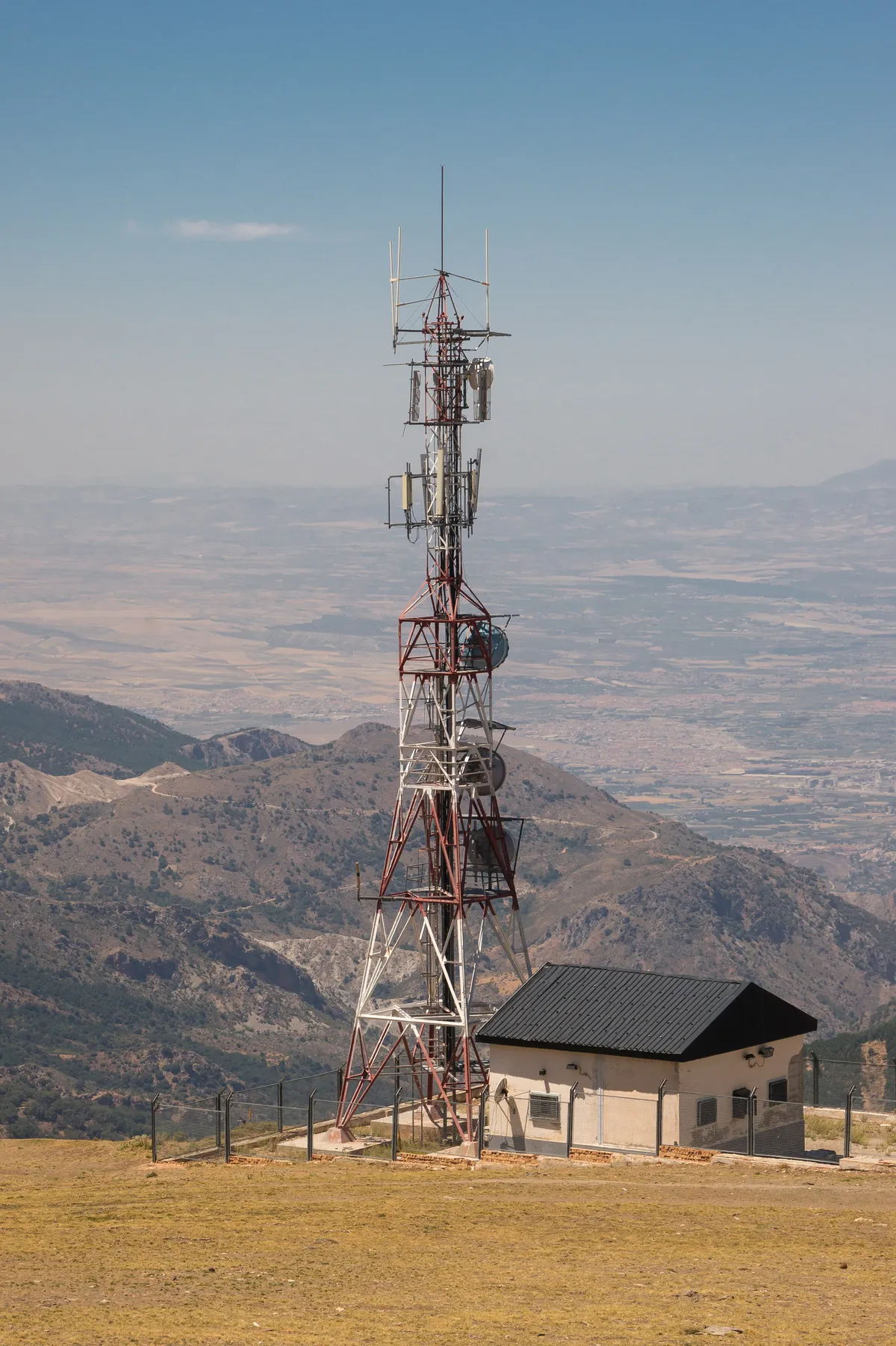 Torre de telecomunicaciones en lo alto de Pradollano (Sierra Nevada) con antenas múltiples sobre celosía metálica blanca y roja, recortada contra el cielo y montañas