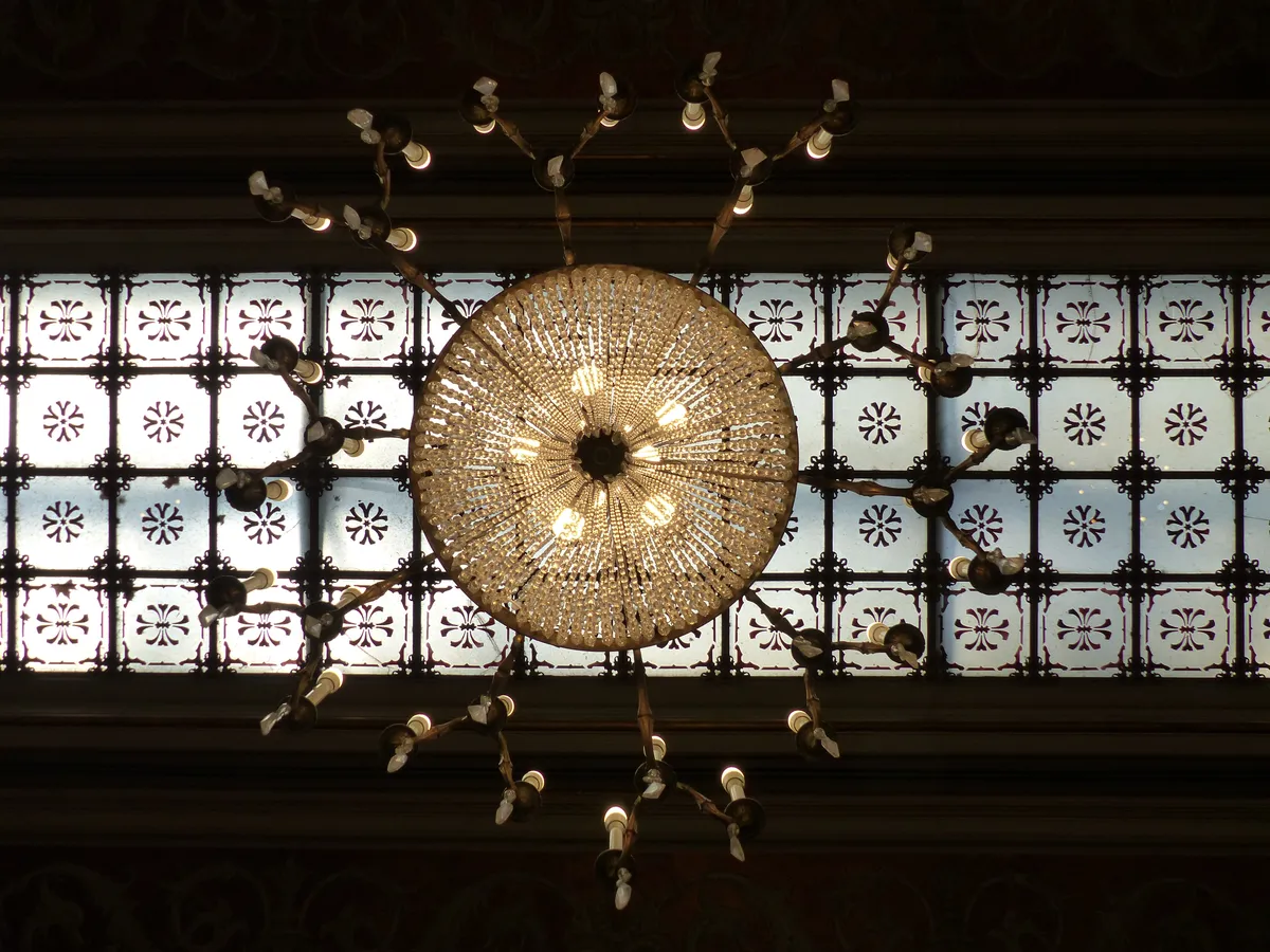 Detalle interior del Palacio de la Bolsa de Madrid: lámpara de araña de cristal sobre vidriera con celosía geométrica