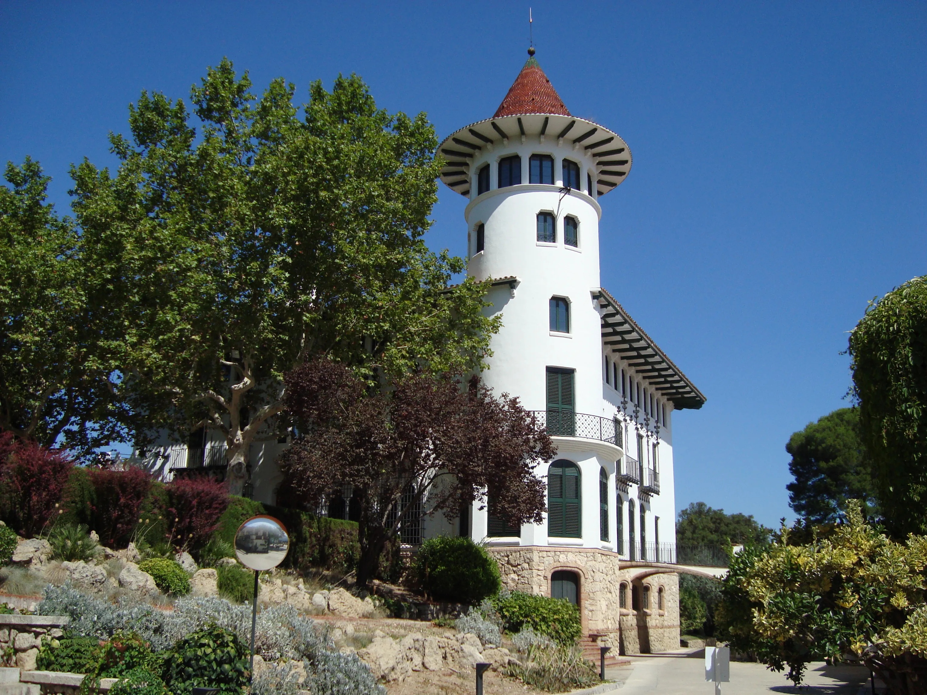 Can Codorníu Chateau, edificio histórico blanco con torre cilíndrica y tejado cónico de teja roja entre vegetación mediterránea